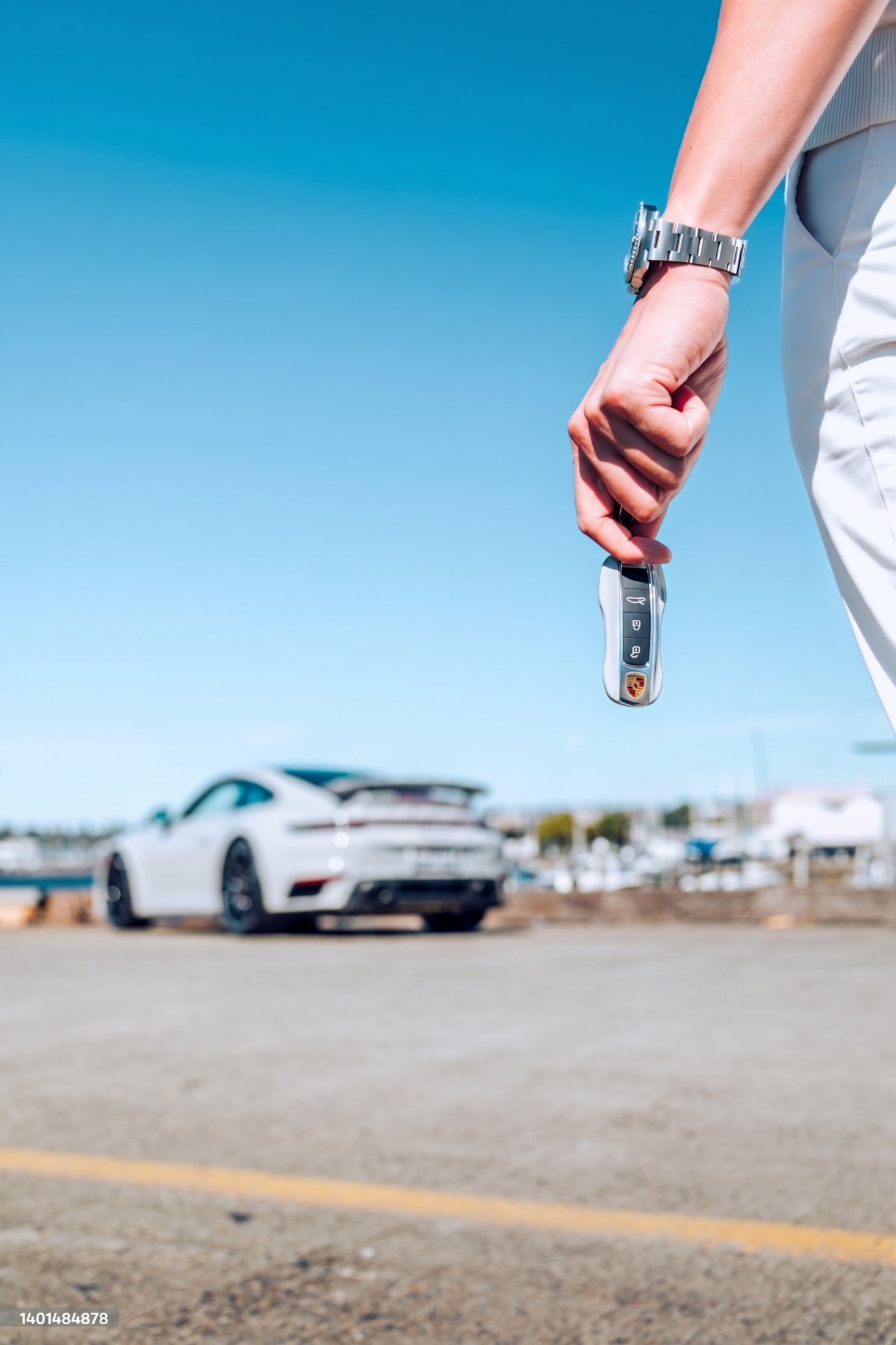 A hand holding a car key fob with the vehicle soft in the background